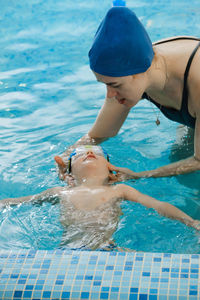 Toddler child learning to swim in indoor swimming pool with teacher. floating in the water