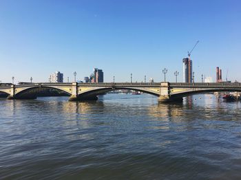 Bridge over river in city against clear blue sky