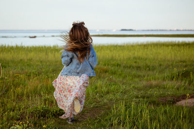 Happy cheerful young woman with long hair running on the grass in nature in a dress