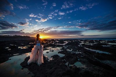 Woman standing on scenic sea against sky during sunset