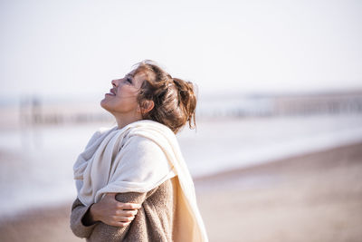 Side view of woman standing at beach against sky