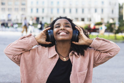 Smiling young with eyes closed listening music through headphones in city