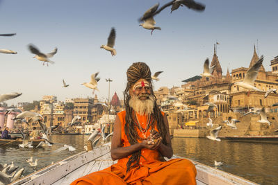 Birds flying over sadhu on boat in sea against sky