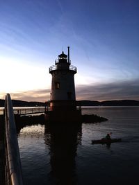 Silhouette lighthouse by sea against sky during sunset