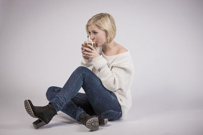 Young woman drinking water from glass against white background