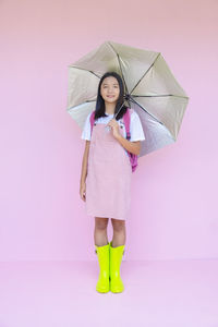 Woman holding umbrella while standing against pink background