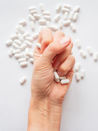 Cropped hand of person holding pills against white background