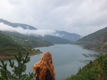 Rear view of woman standing by lake against mountains