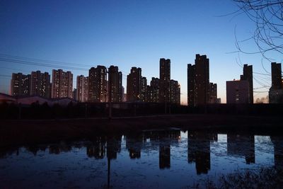 Silhouette buildings by lake against blue sky at dusk