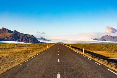 Road leading towards mountains against clear sky