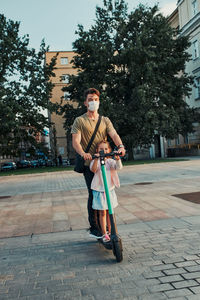 Young man and her sister preschooler riding an electric scooter in the city center