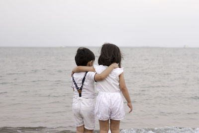 Rear view of friends standing at sea shore against sky