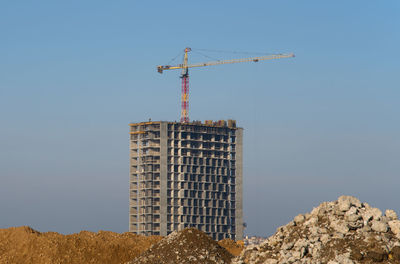 Low angle view of crane by building against clear sky