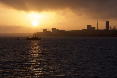 Silhouette city by sea against sky during sunset