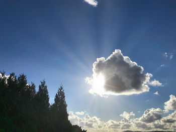 Low angle view of sunlight streaming through clouds
