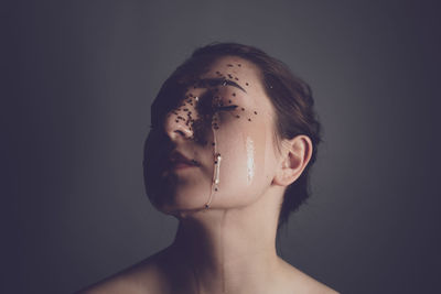 Close-up of shirtless young woman with beauty product on face against gray background