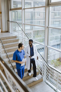 Smiling male doctor and nurse discussing while moving down on staircase in hospital