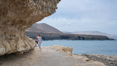 Man standing by cliff at shore against sky