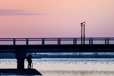 Silhouette people standing by railing against sea during sunset