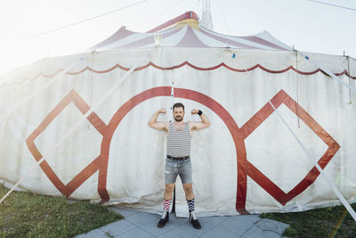 Man showing biceps while standing at circus tent entrance