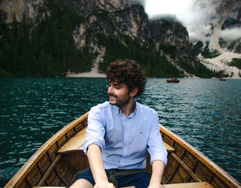 Young man sitting by lake against sky