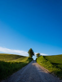 Road amidst field against clear blue sky