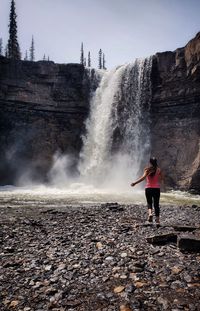 Rear view of woman running towards waterfall against sky