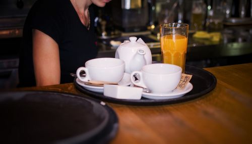 Midsection of woman sitting by dinks in cafe