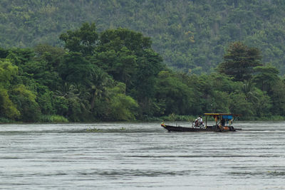 People sailing on river against trees