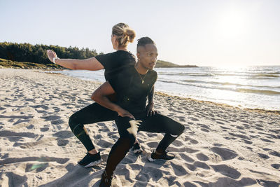 Determined man doing squats with woman on sand at beach