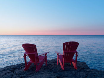 Chairs on beach against sky during sunset