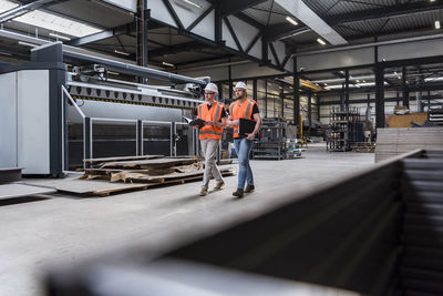 Two men wearing hard hats and safety vests walking on factory shop floor