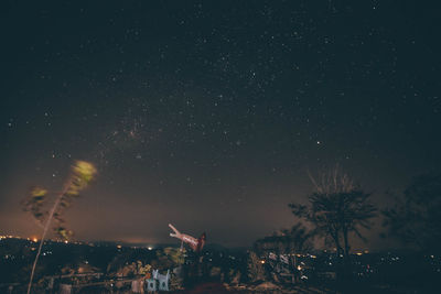 Silhouette trees and illuminated city against sky at night