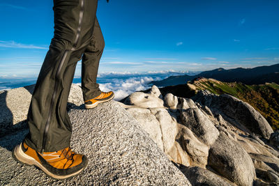 Low section of man standing on rock against sky