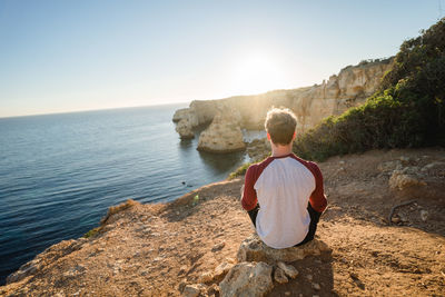 Rear view of man standing on rock by sea