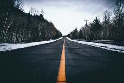 Empty road amidst trees against sky