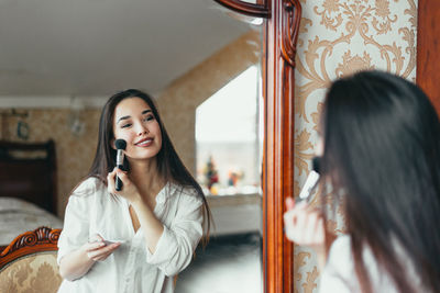 Portrait of beautiful young woman using smart phone in mirror