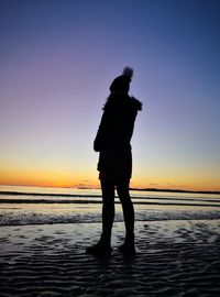 Silhouette man standing on beach against sky during sunset