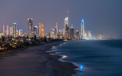 Illuminated modern buildings in city against sky at night