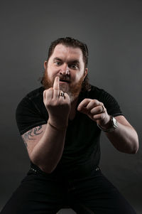 Mid adult man gesturing obscene gesture while sitting against black background