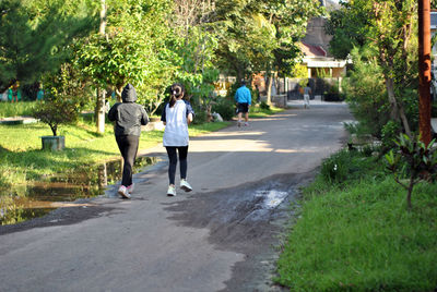 Rear view of people walking on road along trees