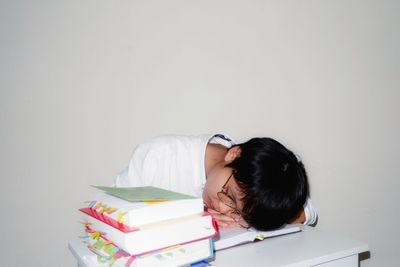 Tired young woman sleeping on books at table against white background