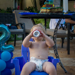 Shirtless boy having drink while sitting on chair