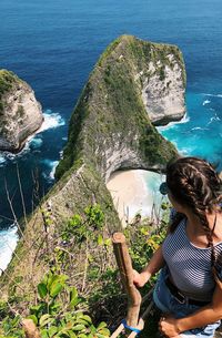 High angle view of young woman looking at sea while standing on mountain during sunny day