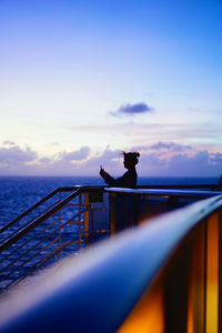 Silhouette railing by sea against sky during sunset