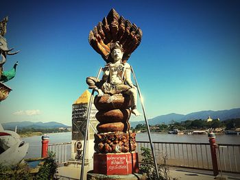 Sculpture by river against clear blue sky