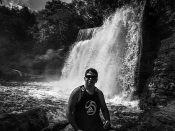 Portrait of young man standing against waterfall