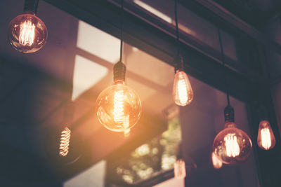 Low angle view of illuminated light bulb hanging at home