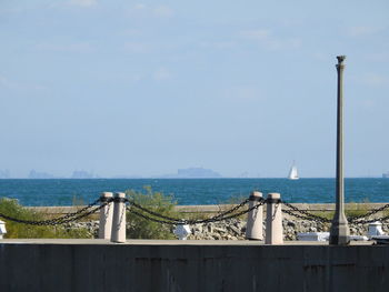 Birds perching on railing by sea against sky