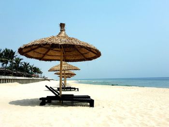 Parasols with deck chairs at beach against clear blue sky